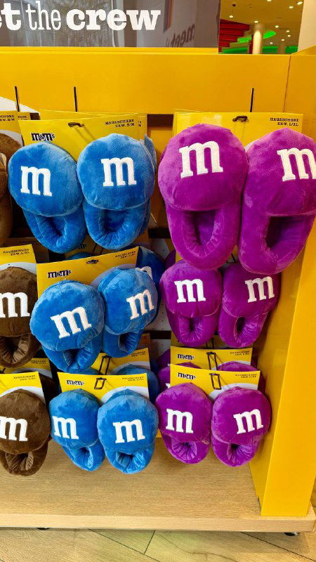 Полки с плюшевыми тапочками и товарами M&M's: яркая витрина с сувенирами, мягкими игрушками и мерчендайзом для всех возрастов.
