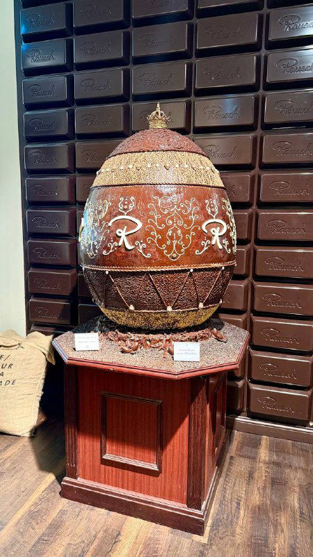 Декорированный огромный шоколадный пасхальный объект или яйцо на выставке Rausch — оформленный экспонат в витрине музея шоколада.