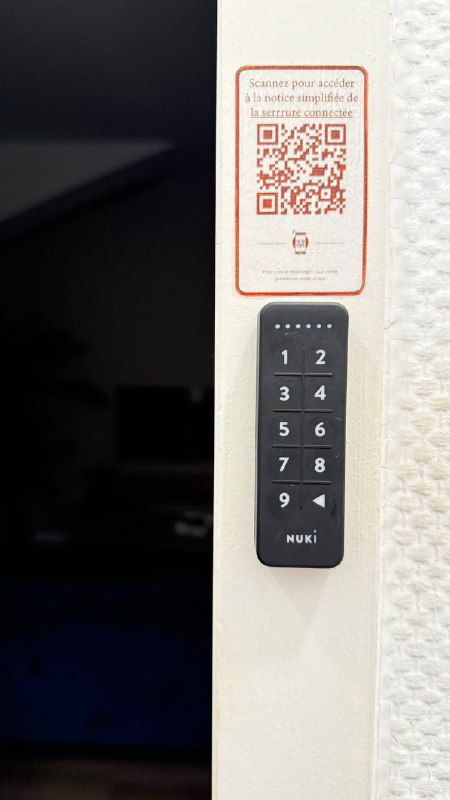 Компактный черный модуль с числовой клавиатурой и наклейкой с QR-кодом на стене — пример способов получения кода доступа к жилью.