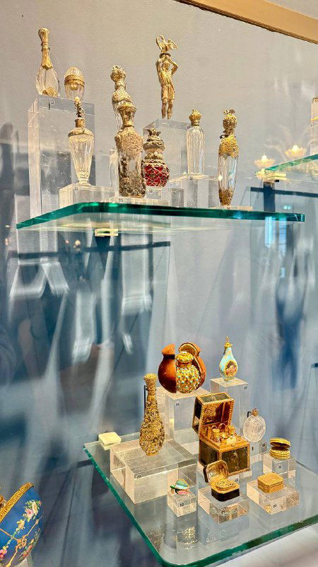 Витрина с коллекцией миниатюрных старинных флаконов для духов, выставленных на стеклянных полках в музее парфюмерии.