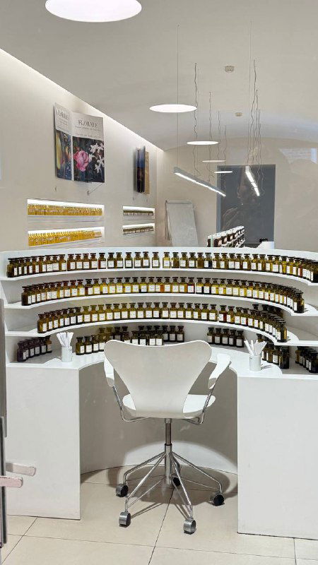 Интерьер мастерской парфюмерии: белые полки, множество флаконов и рабочее кресло перед столом парфюмера в Грассе.