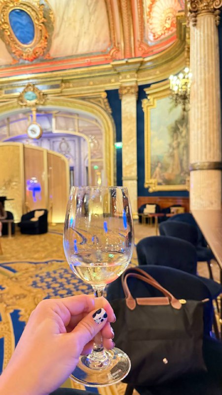 Бокал шампанского в руке на фоне позолоченного интерьера и мягкой мебели — кадр из интерьера заведения в Монако.