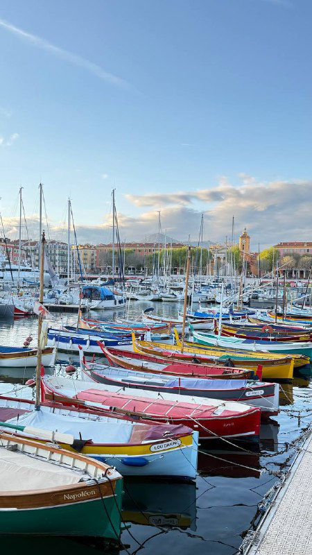 Порт с рядом ярких разноцветных лодок, аккуратно пришвартованных у набережной — типичная прибрежная панорама Лазурного берега.