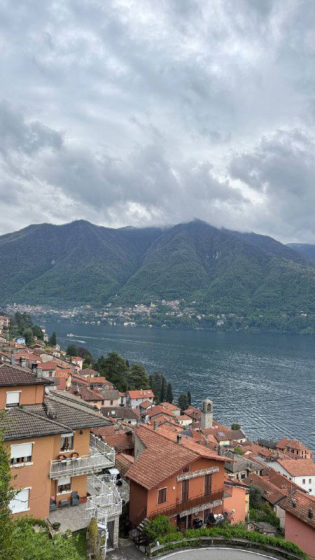 Панорамный вид на крыши домиков, расположенных на склоне над озером Комо; сочетание тёплой плитки крыш и холодной воды создаёт живой городской пейзаж.