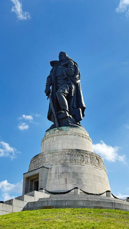 Крупный план гигантской фигуры советского солдата на постаменте против яркого голубого неба — монумент впечатляет размерами и фактурой металла.