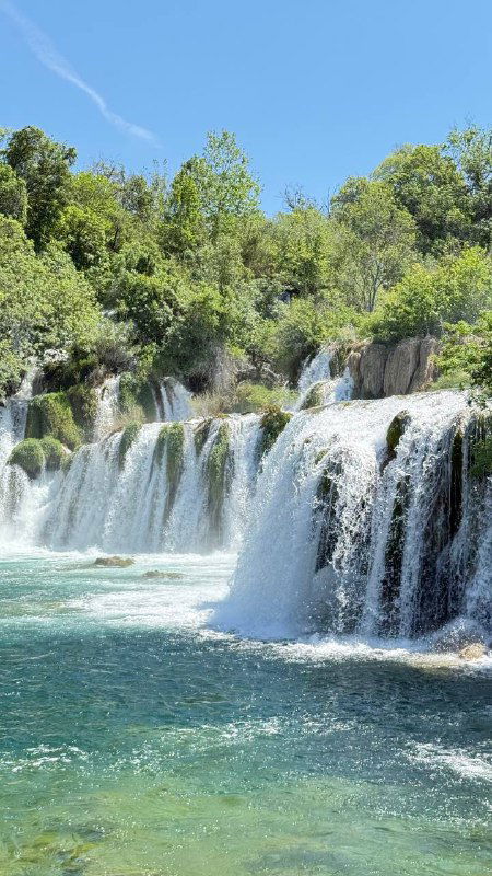 Многоуровневые водопады в густой зелени и изумрудно-голубая вода — панорамный вид национального парка с каскадами и растительностью.