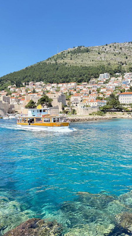 Чистая бирюзовая вода у береговой линии, небольшая лодка у побережья и домики на склоне — типичная сцена хорватского острова с прозрачностью моря.