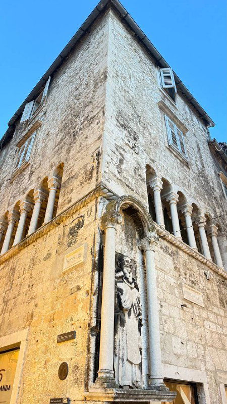 Узкий угол старинного каменного дома с архитектурными деталями и чистым голубым небом — типичный фасад исторического центра города на побережье.