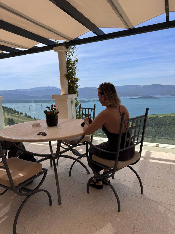 Терраса с видом на море: человек за столиком, бокал вина и расслабленная атмосфера винного бара с видом на залив.