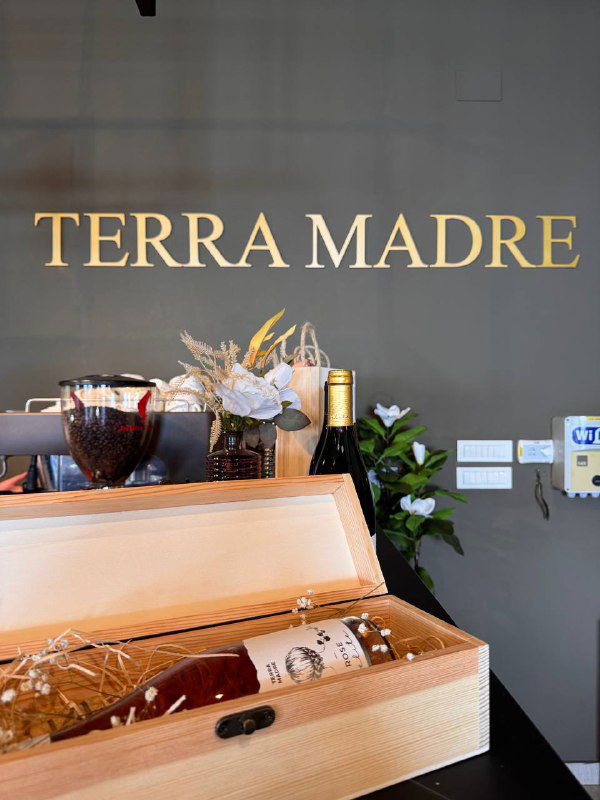 Логотип и оформление Terra Madre на стене, рядом подарочная коробка с бутылкой вина и элементы декора в дегустационном зале.