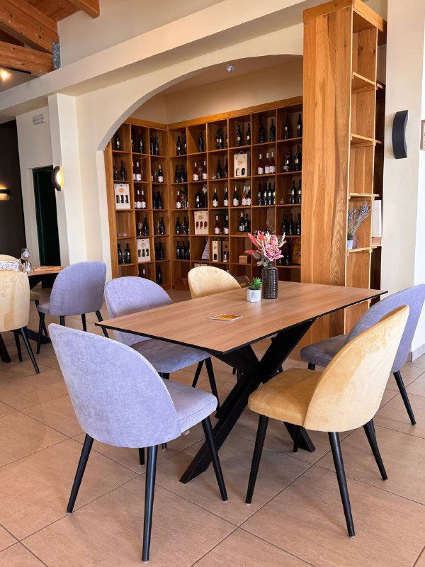 Уютный интерьер ресторана винодельни: деревянные столы и стеллажи с бутылками вина, светлая обстановка для дегустаций и обедов.