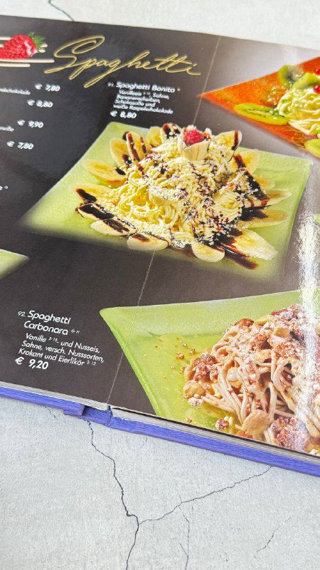 Разворот меню кафе с фотографией десерта «Spaghetti», подписи с ценами и изображениями разных вариантов подачи мороженого, снимок на столе.