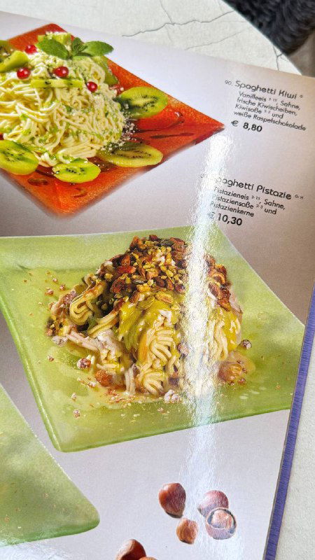 Страница меню с изображениями фисташкового и орехового вариантов спагетти-мороженого на цветных тарелках, вид снизу под углом.