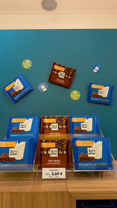 Деревянная витрина в Берлине с образцами Ritter Sport: отдельные квадраты и мини-плитки, рядом ценники и стикеры с информацией о вкусах.