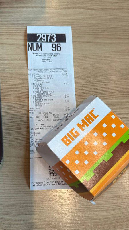 Чек и коробка от Big Mac на деревянном столе: снимок сверху с напечатанным чеком, суммой и фирменной упаковкой бургера, иллюстрация цен в франках.