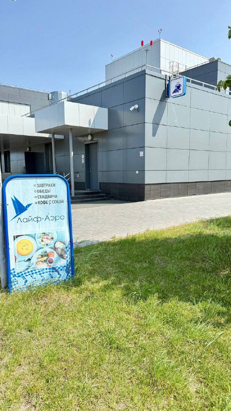 Входная часть современного здания аэропорта «Гагарин» с установкой небольшого рекламного штендера столовой на газоне у фасада терминала.