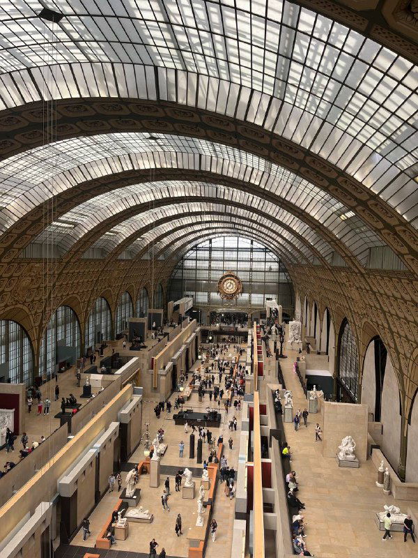 Внутренний простор музея Орсе с высоким стеклянным сводом, посетителями и центральными часами на дальнем плане большого зала