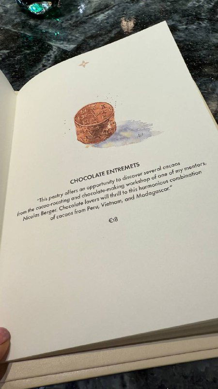 Открытая страница меню или книги с иллюстрацией шоколада в кафе Louis Vuitton: крупный план бумажной страницы и декоративного рисунка