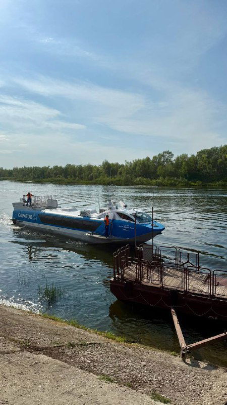 Маленькая моторная лодка пришвартована у заросшего берега Волги, на фоне зелёной прибрежной растительности и спокойной воды речного изгиба.