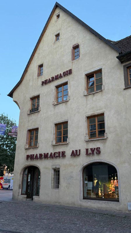 Фасад здания с надписью 'PHARMACIE AU LYS' — здание старейшей аптеки Мюлуза, сохраняющее исторический облик в городской застройке.