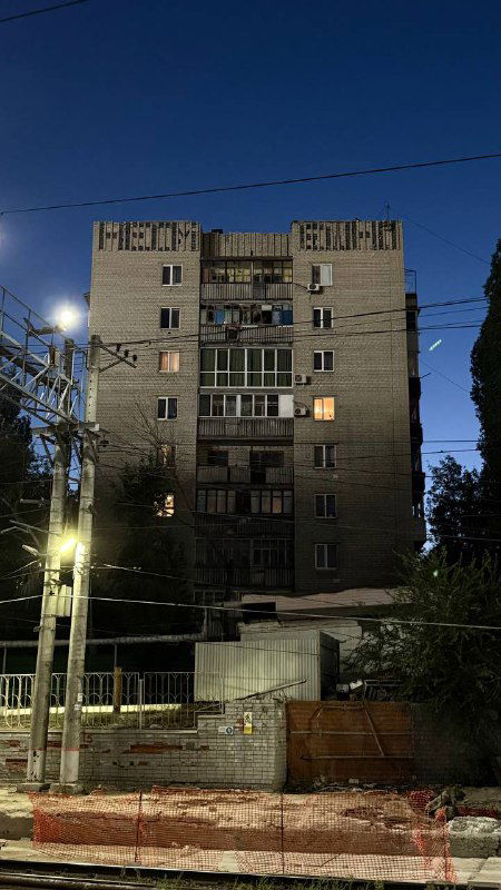 Ночной жилой дом в постсоветском стиле с видимой надписью на фасаде и электрическими линиями — предполагаемый саратовский дом на тёмном небе.