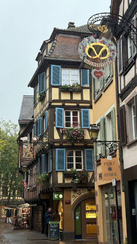 Уютная городская улица с вывесками и декоративными элементами, витрины и многоколорные фасады исторической части Кольмара.