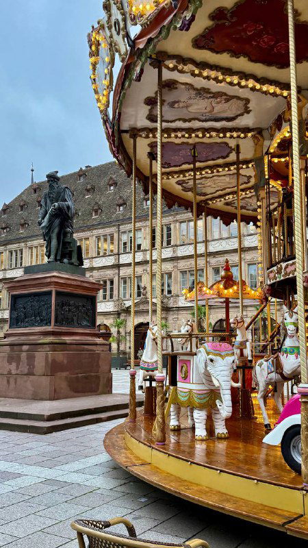 Карусель на площади в Страсбурге на фоне исторической застройки и монумента — атмосферная городская сцена у центральной площади.