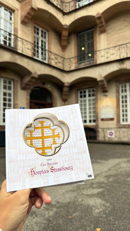 Рука держит визитку или брошюру винного погреба в дворе исторического здания госпиталя — место продажи региональных вин.