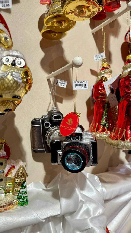 Миниатюрная декоративная камера и золотые украшения, расположенные на салфетке в витрине магазина с разнообразными рождественскими сувенирами.