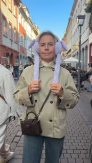 Автор поста на пешеходной улице Гейдельберга в лёгком плаще и шапке, на фоне старых зданий и неба; городской контекст поездки и прогулки.