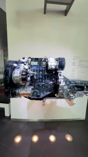 Фрагмент прозрачной модели двигателя и трансмиссии Audi на подставке в музее, показывающий внутреннюю структуру и рабочие узлы в разрезе для наглядной демонстрации.