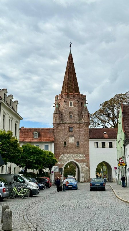 Вид на одну из старых городских ворот Ингольштадта, историческая кирпичная башня и прилегающие здания, показывающие атмосферу хорошо сохранившегося старого города.