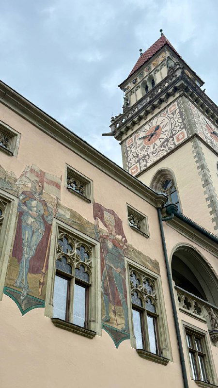 Средневековая башня с часами и расписными фасадами в Пассау: архитектурные детали и каменная кладка на близком плане под серым небом.
