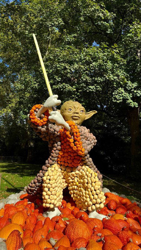 Фигура, напоминающая персонажа в образе воина с мечом, собранная из множества тыкв разнообразных размеров и оттенков в садовой зоне фестиваля.