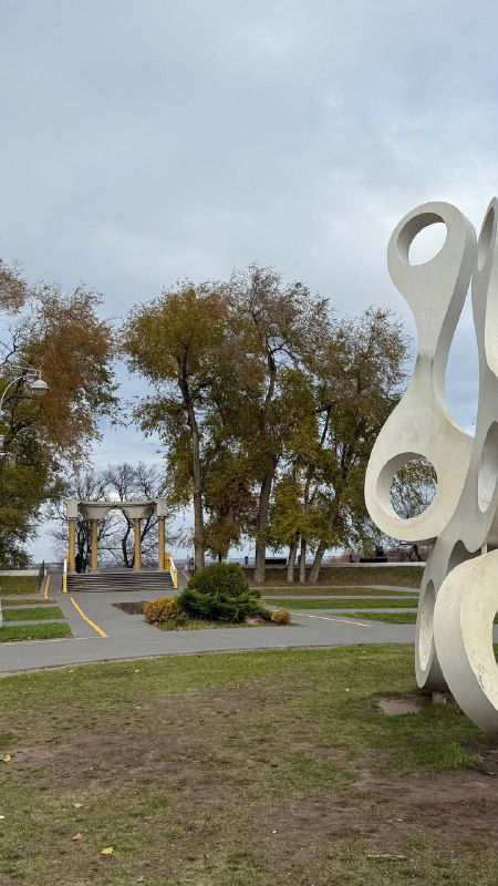 Пейзаж городского парка и декоративная скульптура: дорожки, деревья и архитектурные элементы на фоне неба в центре Энгельса.