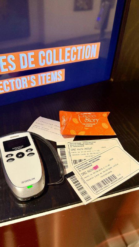 Аудиогид и билет с дегустационным набором на стойке при входе: устройство аудиогида, бумажные билеты и карточка дегустации вблизи.