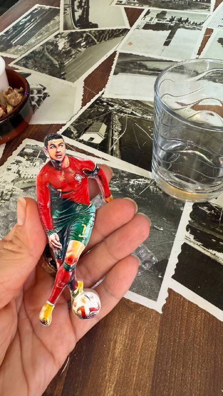 Фигурка футболиста в руке автора на фоне столешницы с футбольными карточками и следами дегустации напитков.