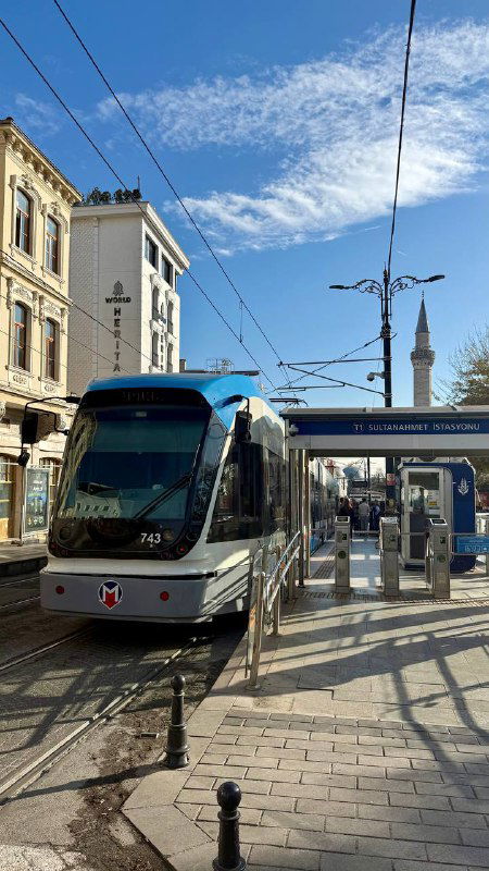 Современный трамвай линии T1 на городской остановке Стамбула: рельсы, столбы и характерная городская инфраструктура под ясным небом.