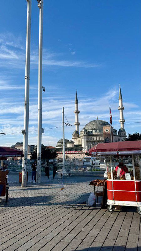 Набережная у мечети с прибрежными тележками и видом на купола: утренний городской пейзаж и торговые палатки рядом с причалом.