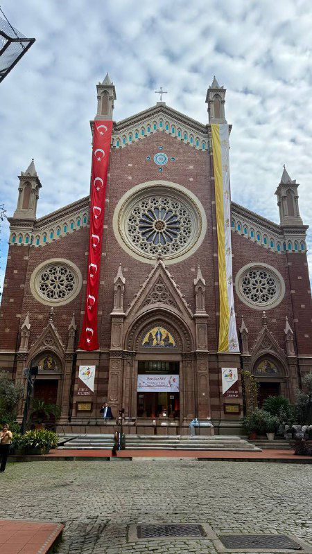 Фасад западной церкви в Стамбуле, украшенный флагами и розовым кирпичом, пример архитектурного разнообразия города и туристических точек.