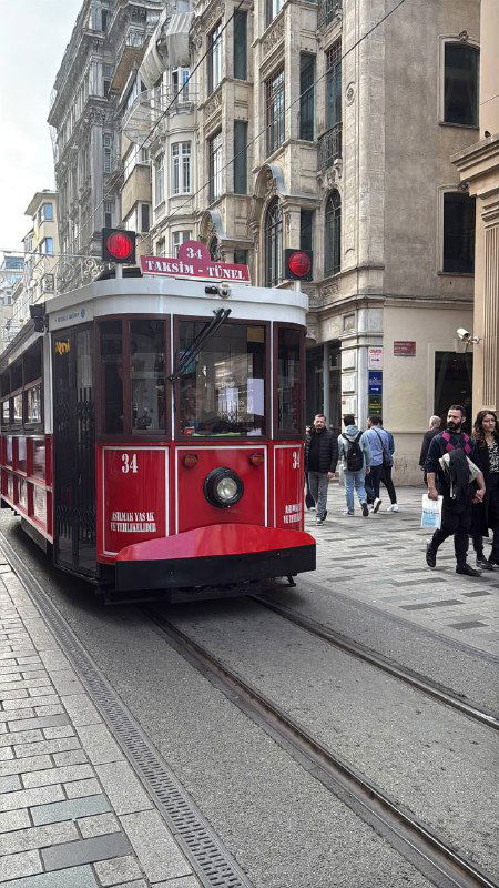 Красный ретро-трамвай едет по пешеходной улице Истикляль в Стамбуле: рельсы, прохожие и уличная жизнь в центре города, атмосфера прогулки.