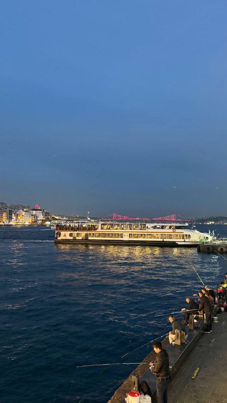 Паром на фоне ночной бухты и огней города в Стамбуле: вид с Галатского моста на паромы и набережную в вечернем свете.