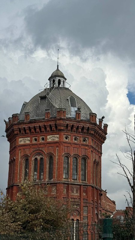 Кирпичная круглая башенка старого здания на фоне облачного неба — историческая часть района, контрастирующая с яркими домами.