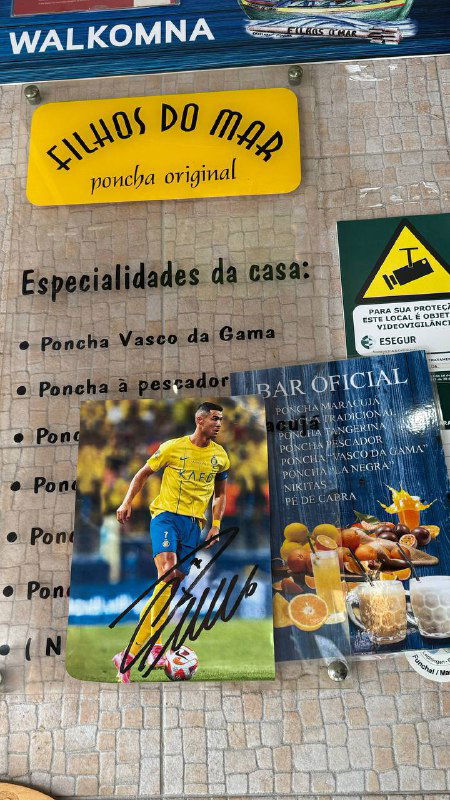 Стена с меню и рекламой пончи, видна табличка «Filhos do Mar» и карточки с автографами — атмосферный уголок бара Камара‑ди‑Лобуш.