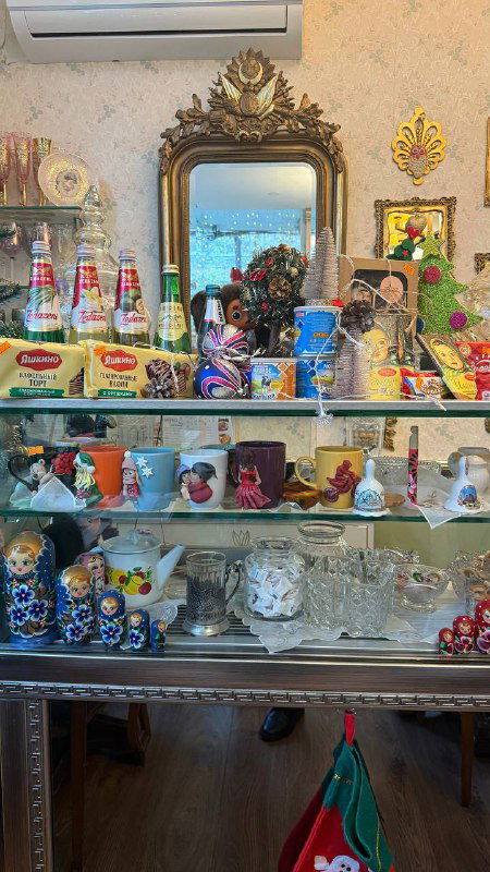 Витрина с русскими сладостями и товарами: матрёшки, банки сгущёнки и разноцветные упаковки на стеклянных полках в кафе-лавке.