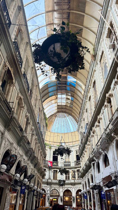 Внутренний вид крытого пассажа с высоким стеклянным куполом и праздничной декорацией, просторный коридор между рядами магазинов и кафе.