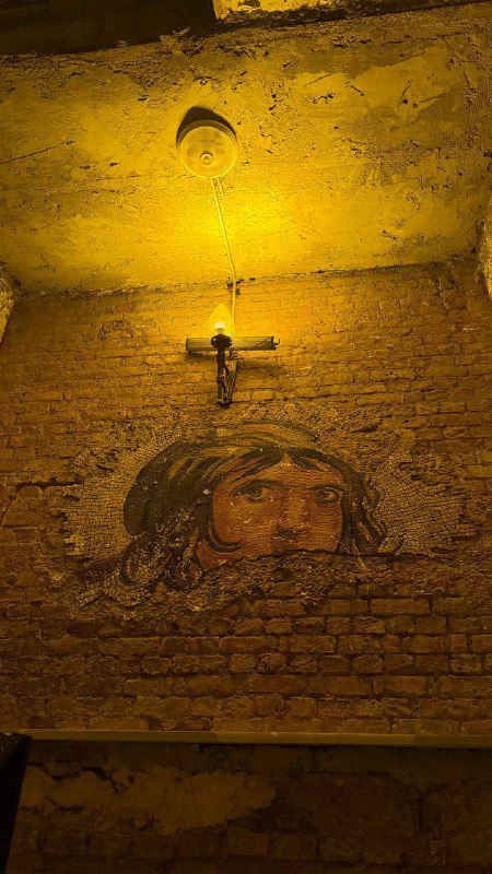 Крупный план настенной мозаики или изображения в подземной части Rumeli Han — лицо на кирпичной стене при тёплом боковом свете.