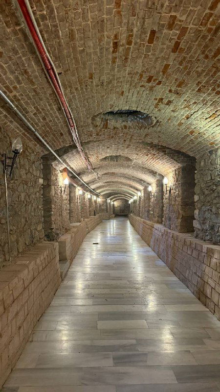 Длинный коридор подземной галереи с арочными сводами и плиточным полом, перспективный вид вдоль туннеля Rumeli Han, ощущение подземного пространства.