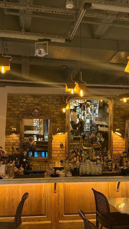 Интерьер кофейни с деревянной барной стойкой, зеркалами и тёплым освещением — уютная атмосфера для кофе и десертов в Pera.