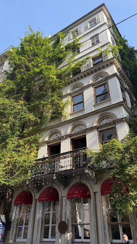 Высокий исторический дом в Pera с балконами и зеленью на фасаде — архитектурный городской вид рядом с улицей Истикляль.